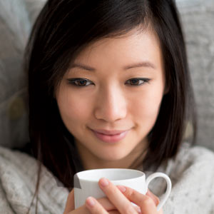Woman on couch after using DialCare under blanket smiling holding cup of hot tea